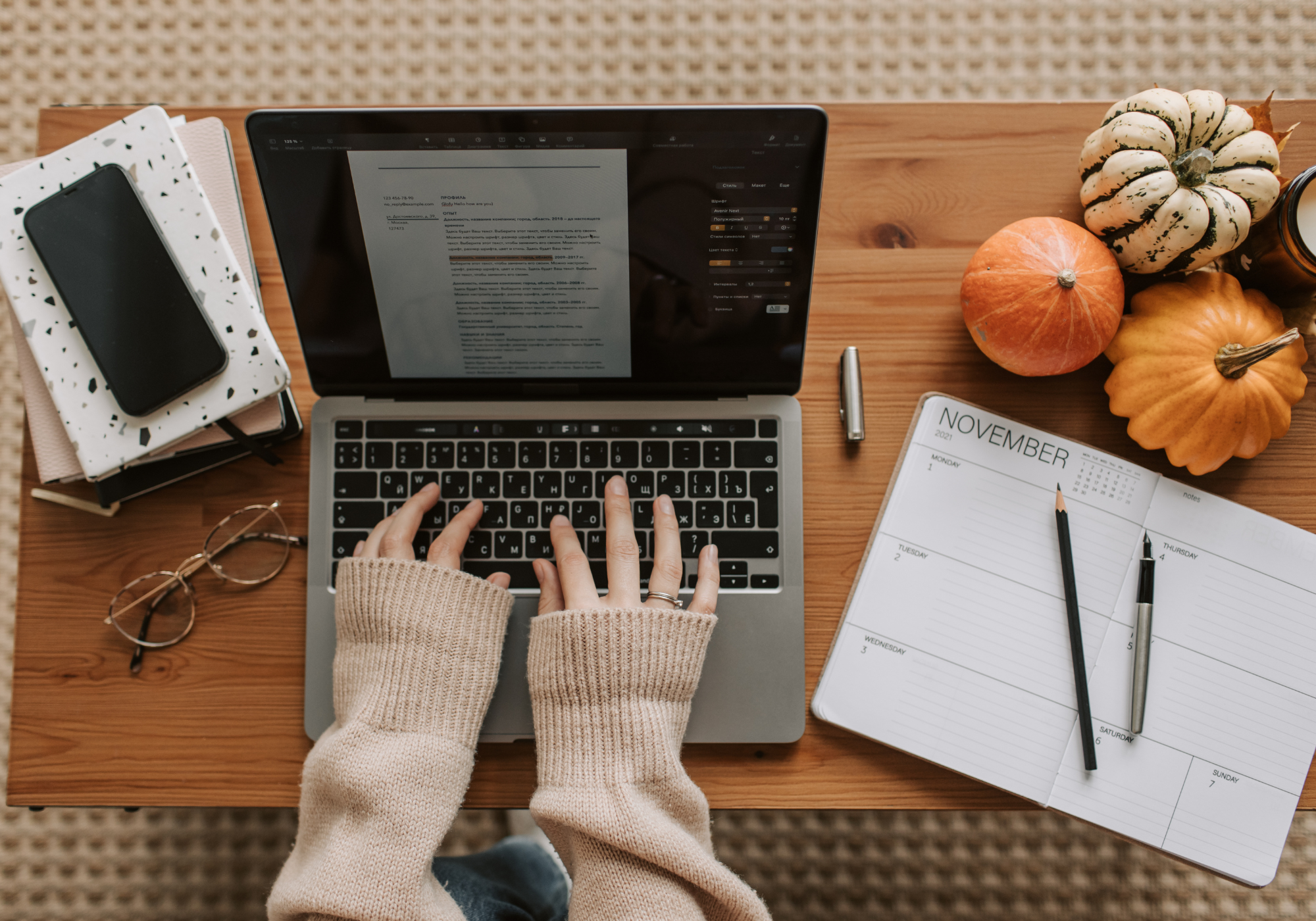 Person working on a laptop at a desk with a planner and fall decorations.